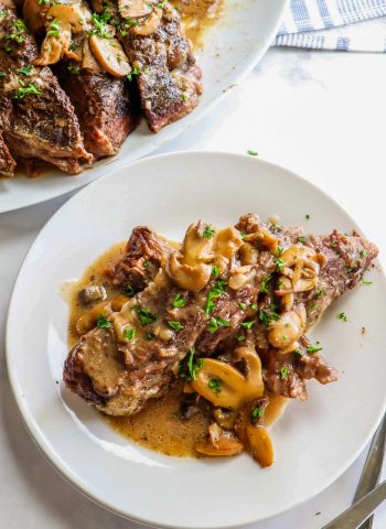 An overhead picture of pot roast with mushrooms on a white plate and a platter of pot roast in the background.