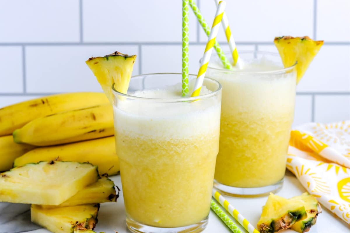 A picture of two glasses  filled with the smoothie with straws in them and a pineapple slice.