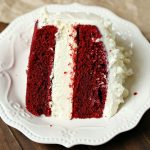 A close up picture of a slice of red velvet cheesecake on a white plate.