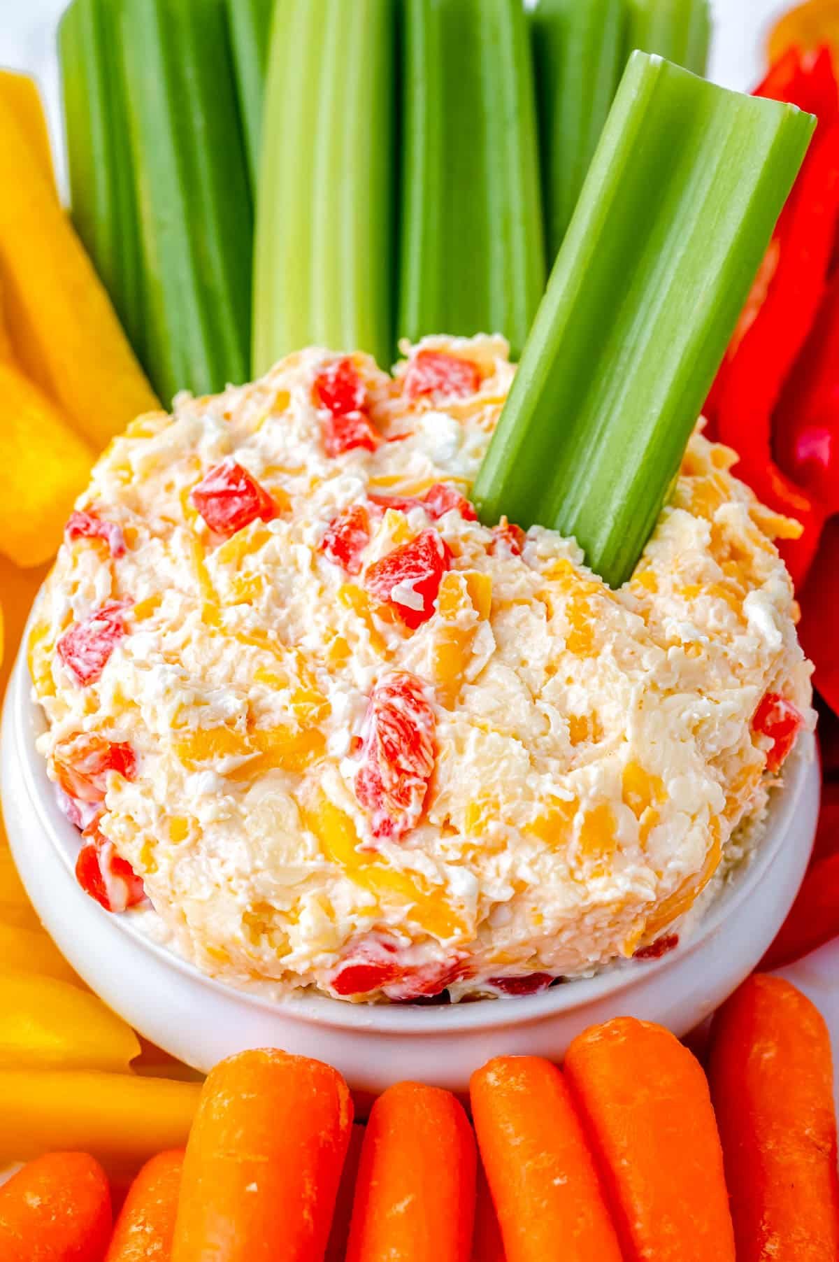 The finished Pimento Cheese recipe in a white serving bowl surrounded by veggie sticks.