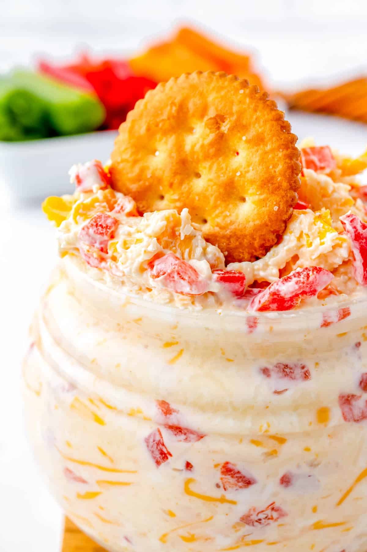 A close up picture of the Pimento Cheese in a serving jar and a cracker dipped into it.