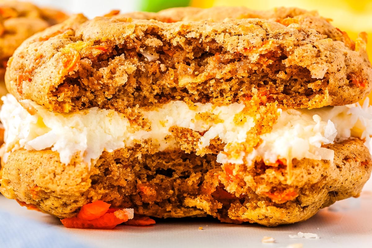 A close up picture of a carrot cake whoopie pie with a bite taken out of it.