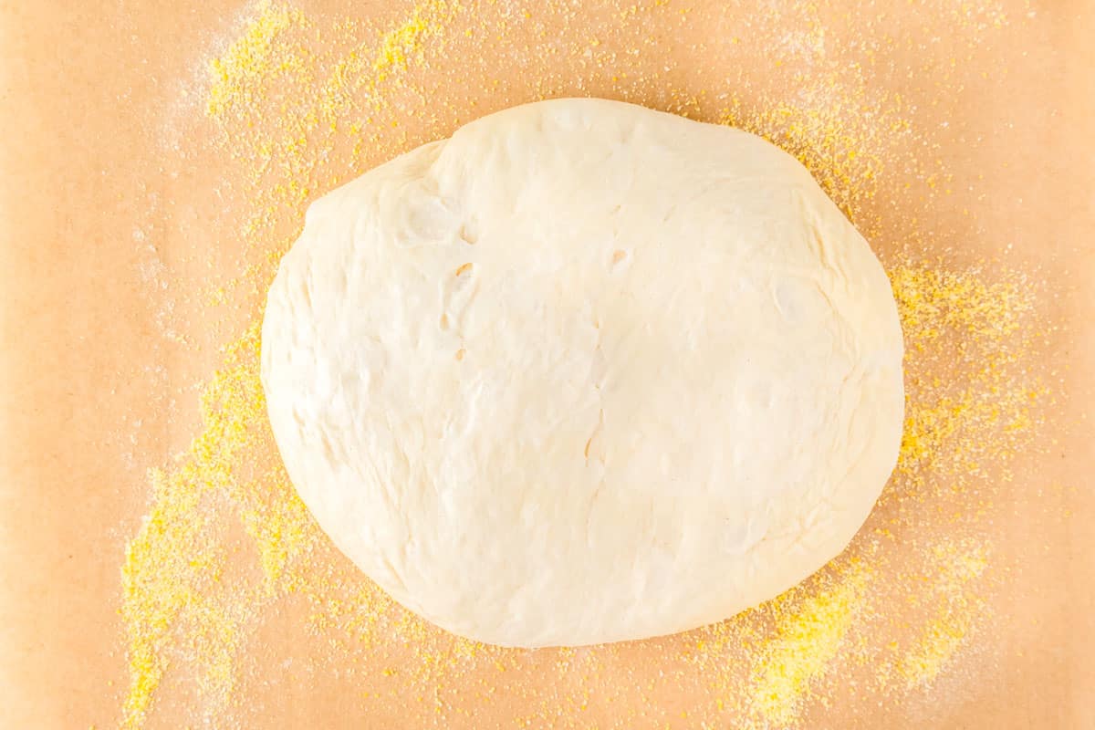 A dough ball on a piece of parchment with cornmeal.