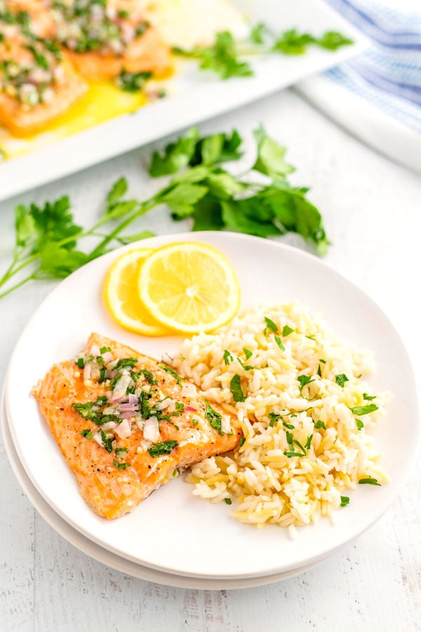 A white dinner plate with baked salmon, rice pilaf, and lemon slices on it.