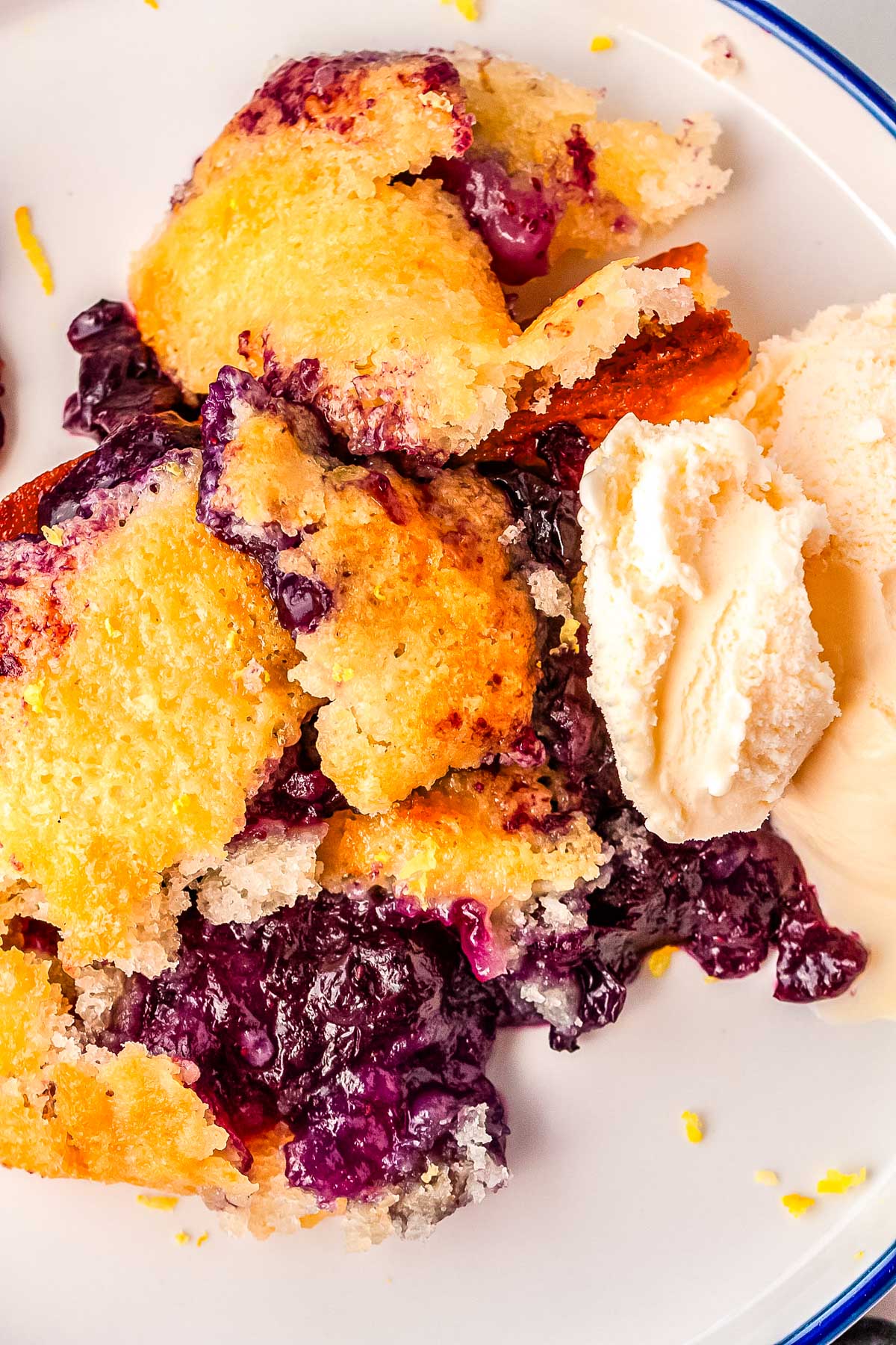 Scoops og blueberry lemon cobbler on a plate and garnished with ice cream and lemon zest.