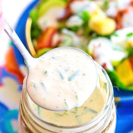 A ladle of buttermilk ranch coming from a mason jar full of dressing.