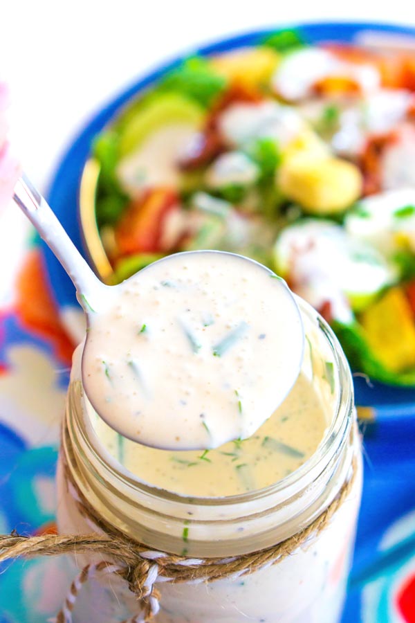 A ladle of buttermilk ranch coming from a mason jar full of dressing.