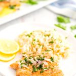 A baked salmon fillet on a white plate with rice pilaf and lemon slices.