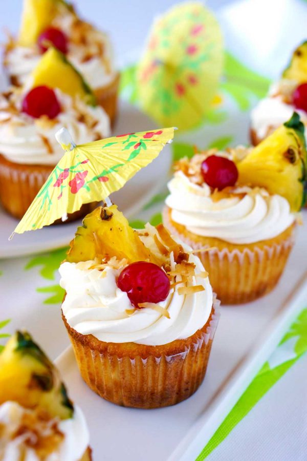 Pineapple and coconut frosting garnished with paper drink umbrellas, coconut, pineapple, and cherries.