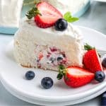 A picture of a slice of the cake on a plate with strawberries and blueberries as garnishes.