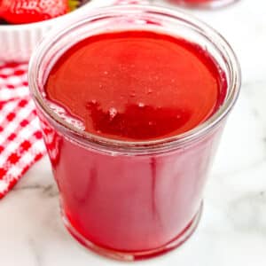 A close up of Strawberry Syrup in a glass jar.