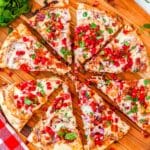 The strawberry pizza cut into slices on a wood board.