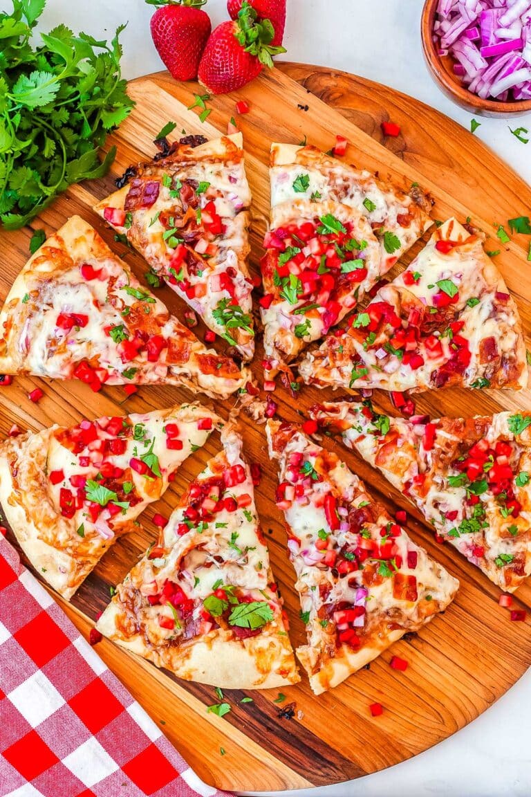 The strawberry pizza cut into slices on a wood board.