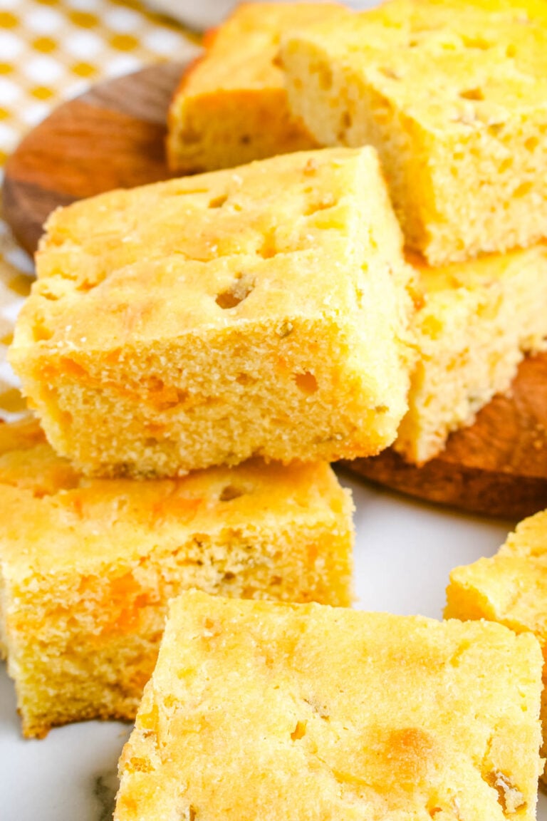 Cheesy green chile cornbread squares stacked on a wooden board showing the soft crumb and melted cheddar inside.