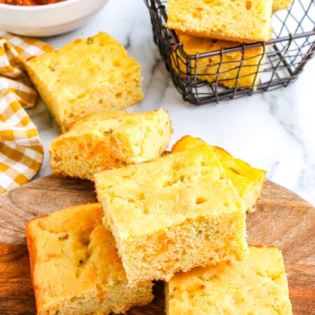 Cheesy green chile cornbread served with a bowl of chili and stacked cornbread squares in a basket.