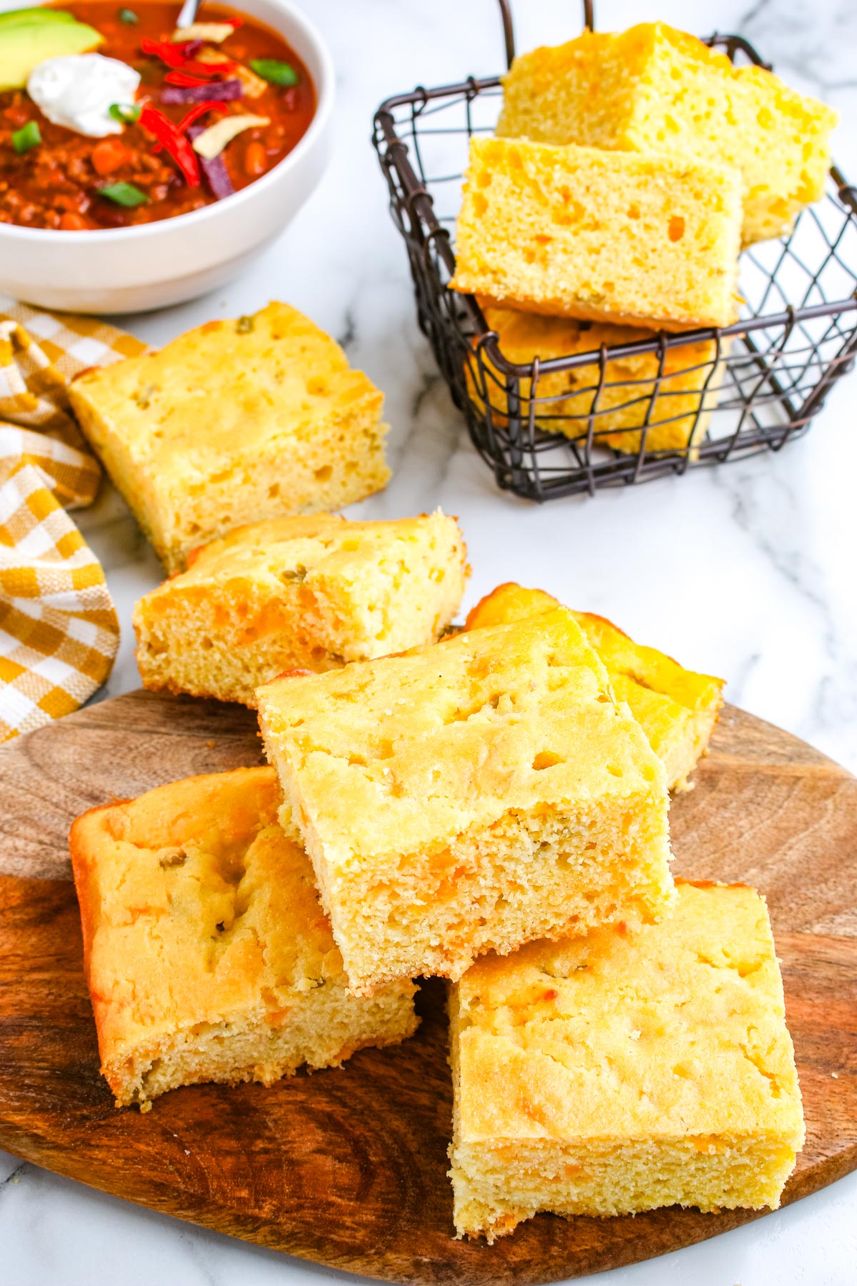 Cheesy green chile cornbread served with a bowl of chili and stacked cornbread squares in a basket.