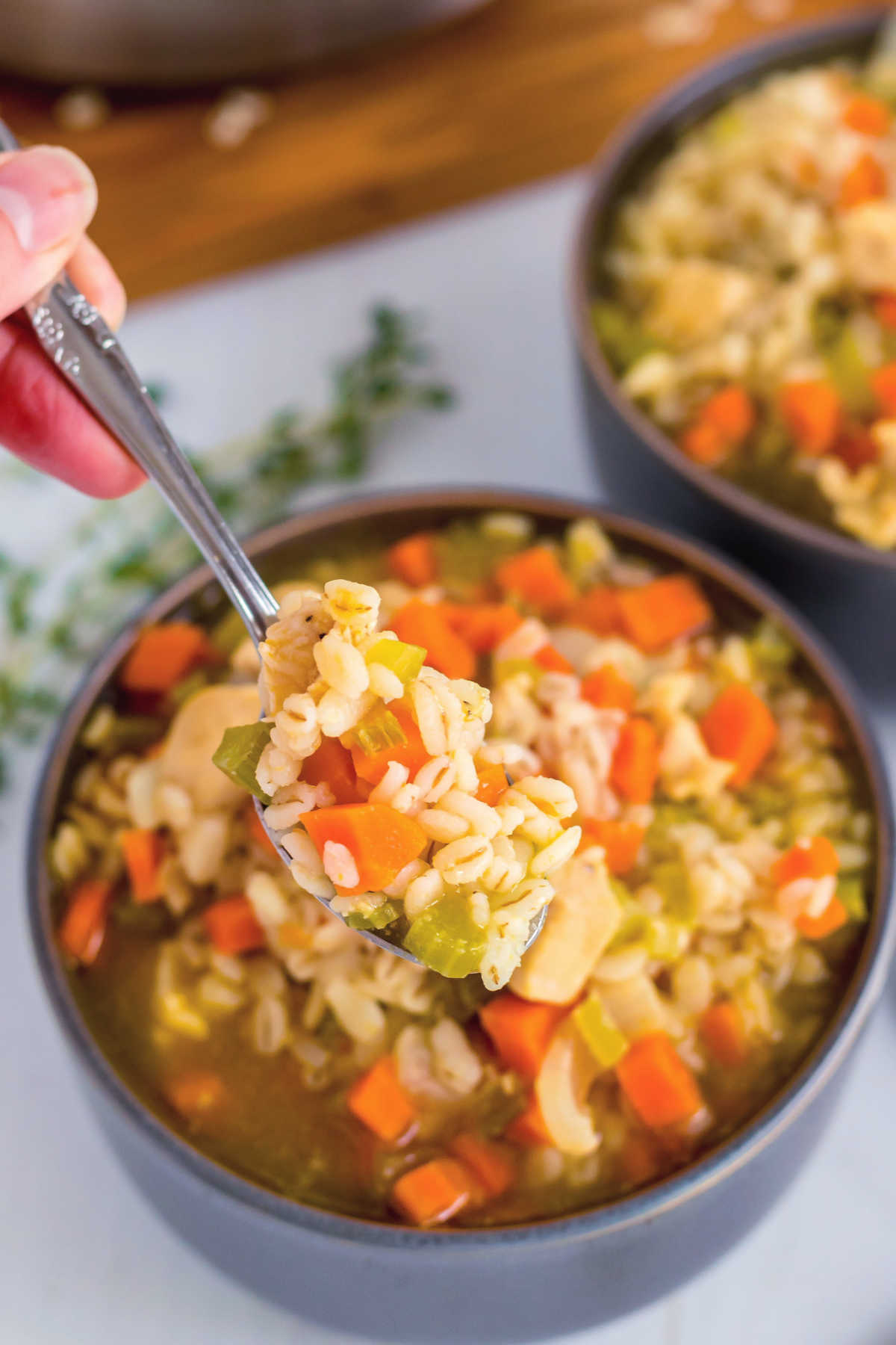 A spoon listing up some Chicken Barley Soup. 
