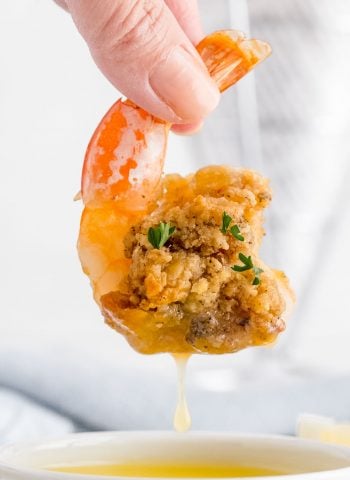 A baked stuffed shrimp being dipped into melted butter.