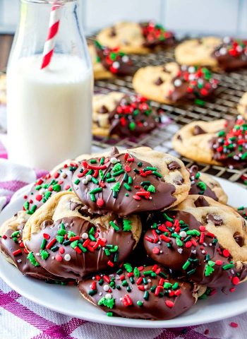 Dipped Christmas Chocolate Chip cookies on a plate with Christmas sprinkles.