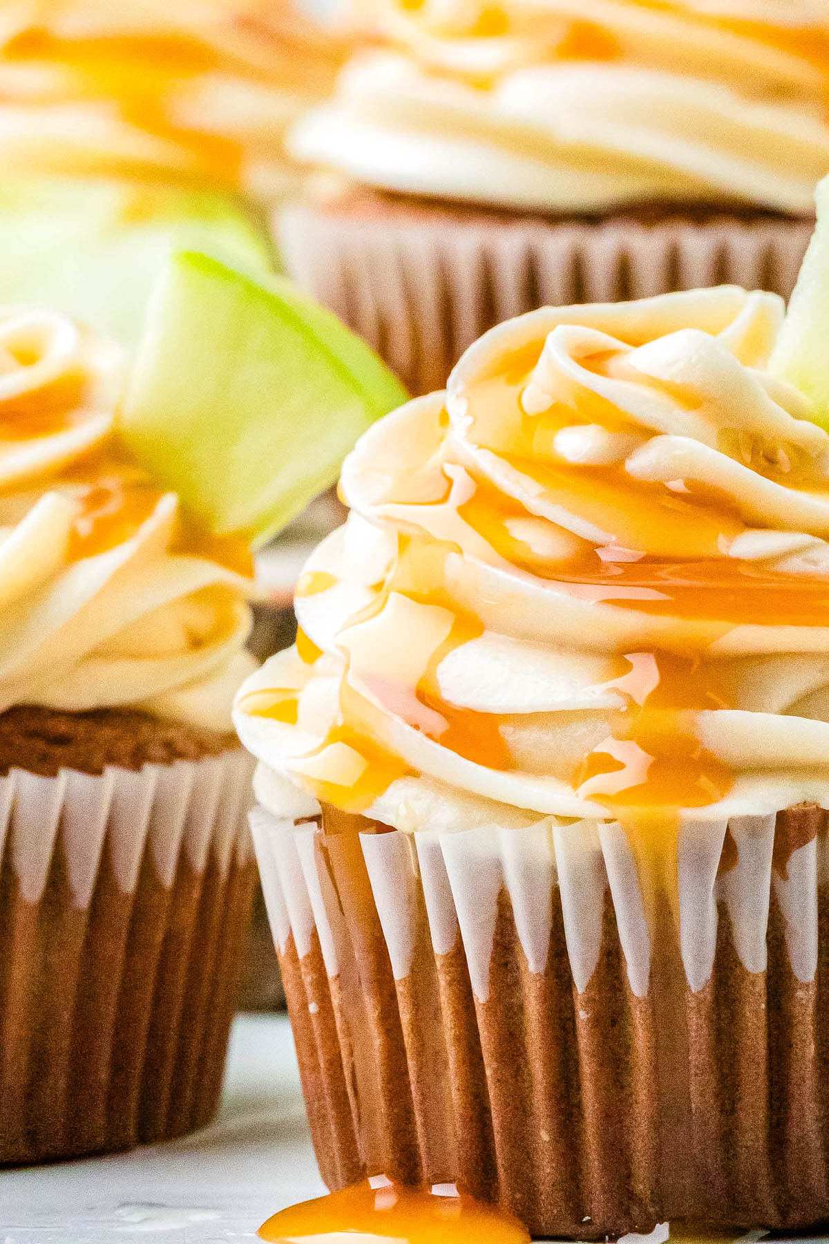 Close-up of a caramel apple cupcake with caramel buttercream frosting, caramel drizzle, and a slice of green apple on top.