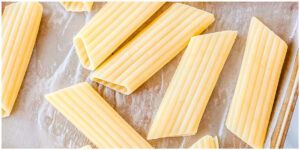 Uncooked manicotti pasta tubes arranged on parchment paper before filling.