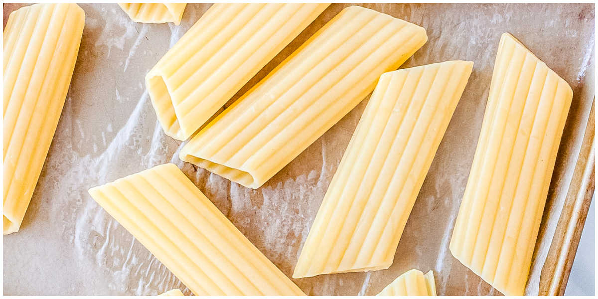 Uncooked manicotti pasta tubes arranged on parchment paper before filling.