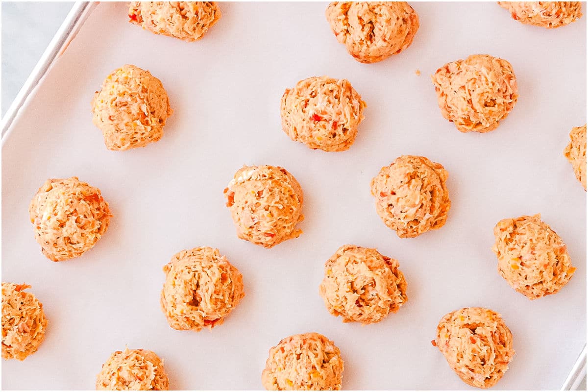 The sausage balls on a rimmed baking sheet before thy've been cooked.