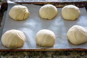 Place the dough balls on a greased piece of parchment and over and rest the dough.