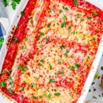Overhead view of baked three cheese manicotti in white casserole dish garnished with parsley.