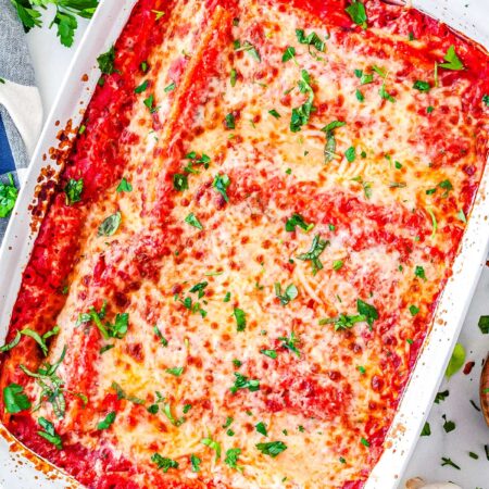 Overhead view of baked three cheese manicotti in white casserole dish garnished with parsley.