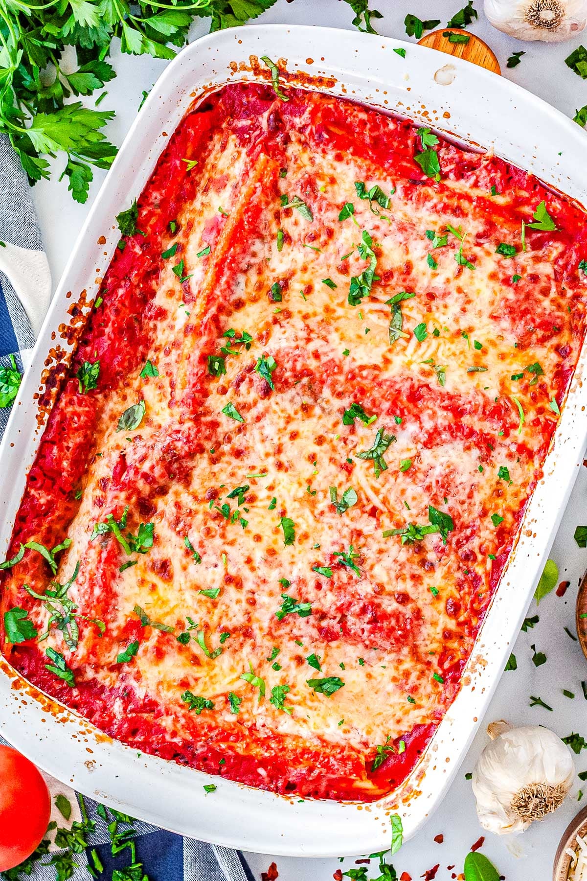 Overhead view of baked three cheese manicotti in white casserole dish garnished with parsley.