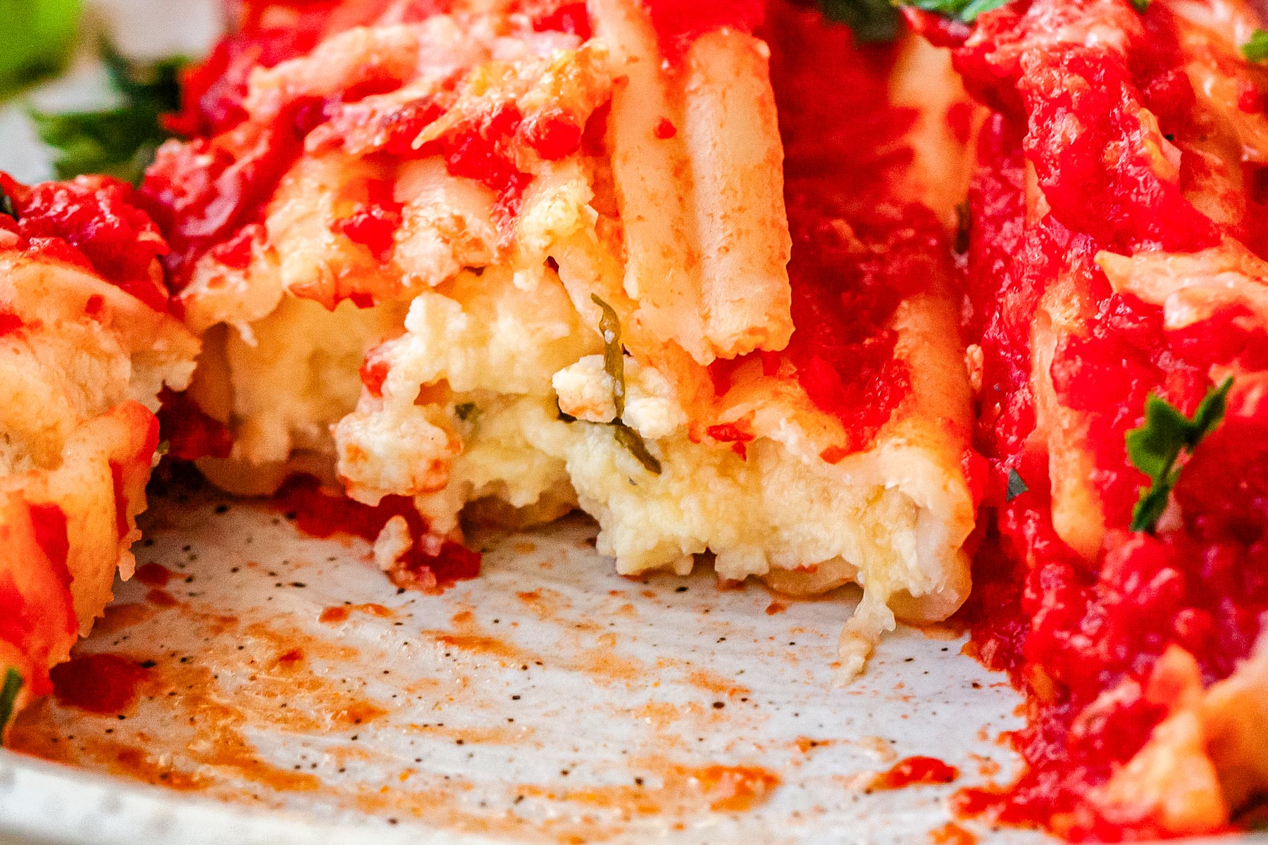 Close up of manicotti showing creamy ricotta and herb filling inside pasta shell.