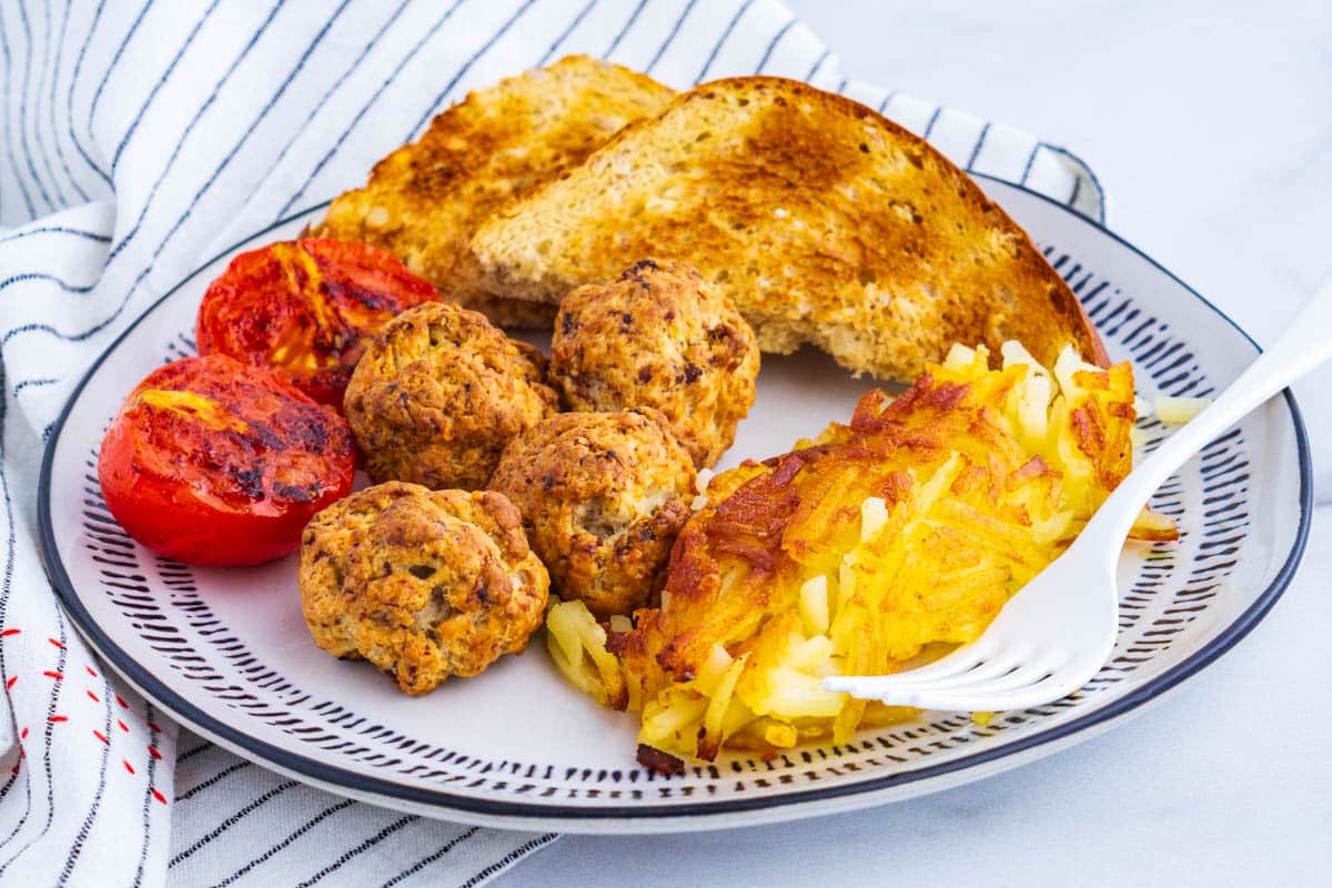 The finished sausage balls recipe on a breakfast plate with hashbrowns, toast, and tomatoes.