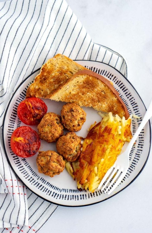 Sausage and cheese balls served for breakfast with a plate of toast, hash browns, and cooked tomato halves. 