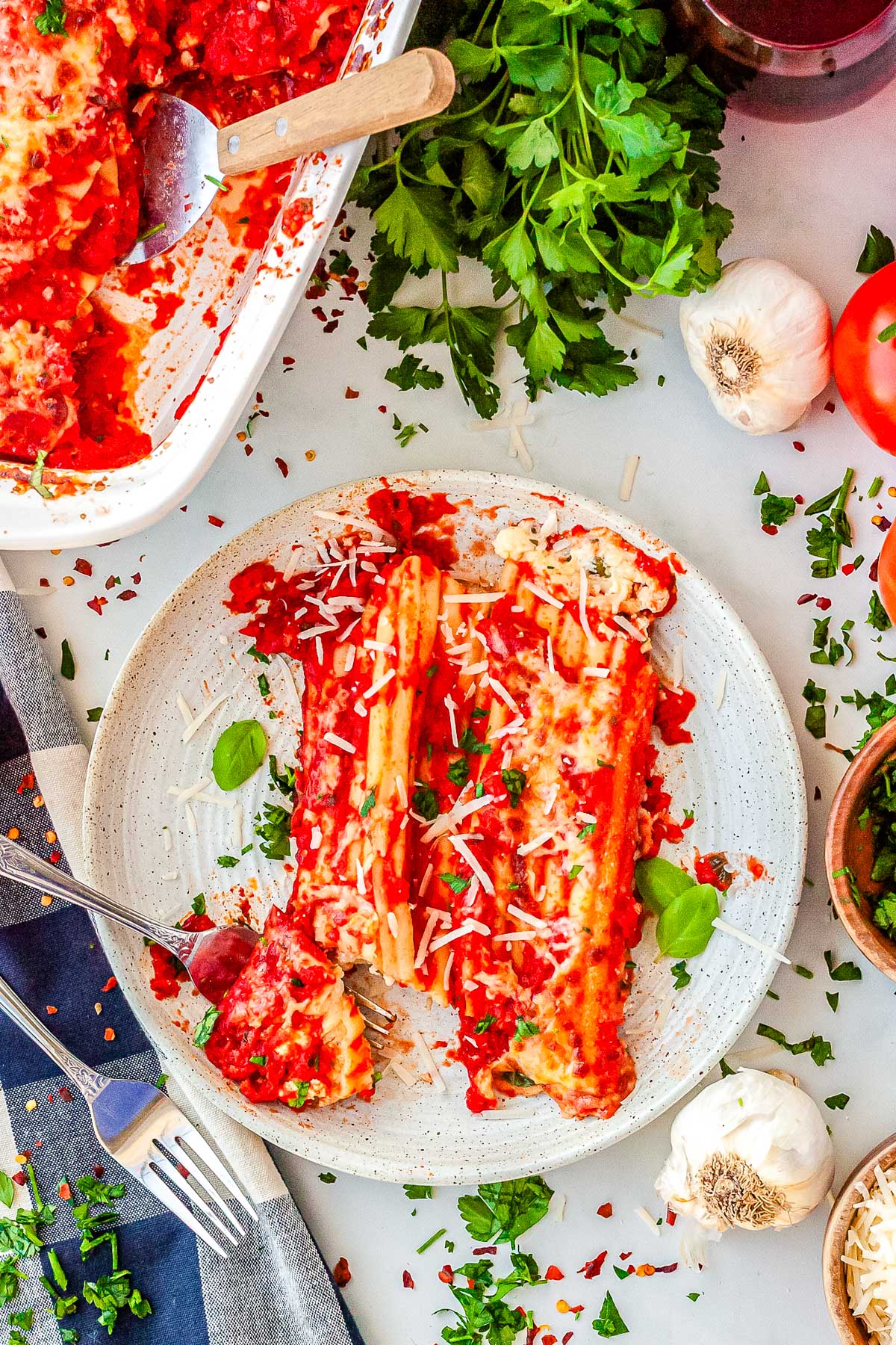 Serving of three cheese manicotti on a plate topped with marinara sauce, Parmesan, and fresh herbs.