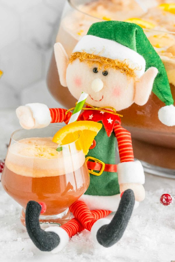A cute stuffed elf sipping on a glass of non-alcoholic Christmas Punch. 
