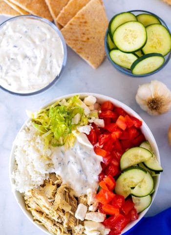 Gyro bowl with rice, slow cooker chicken, tomatoes, bell pepper, cucumber, shredded lettuce, feta, and pita triangles.