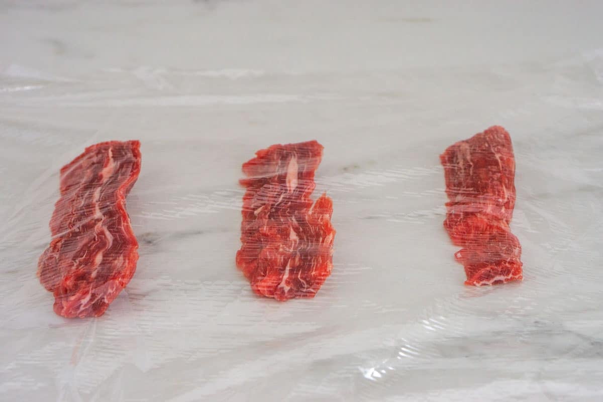 Three slices of steak under plastic wrap ready to be pound thin.