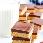 Three No-Bake Chocolate Peanut Butter Bars stack on top of each other with a glass of milk in the background.