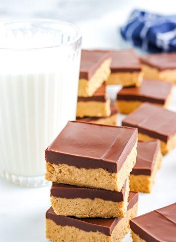 Three No-Bake Chocolate Peanut Butter Bars stack on top of each other with a glass of milk in the background.
