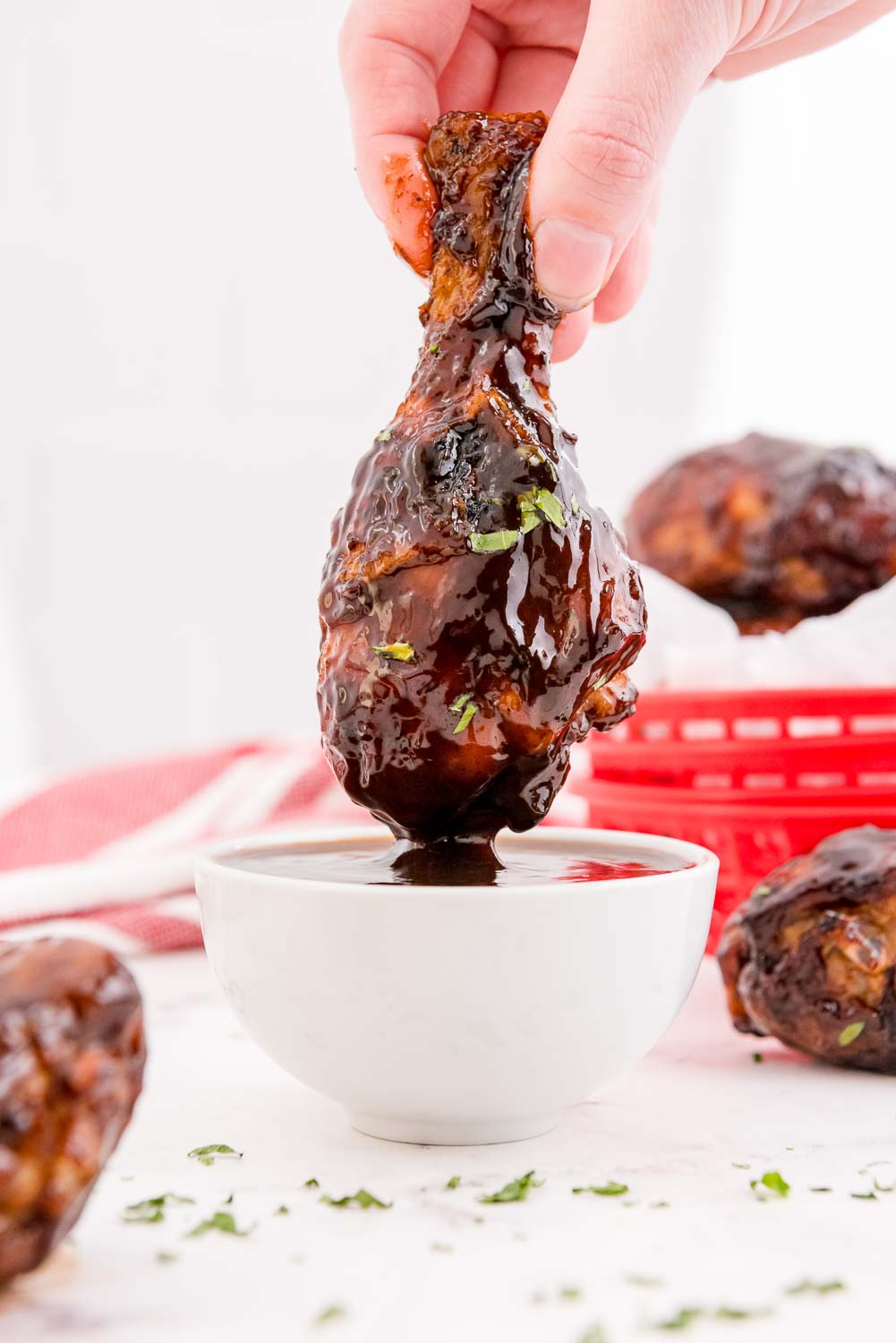 An oven baked BBQ drumstick being dipped in BBQ sauce.