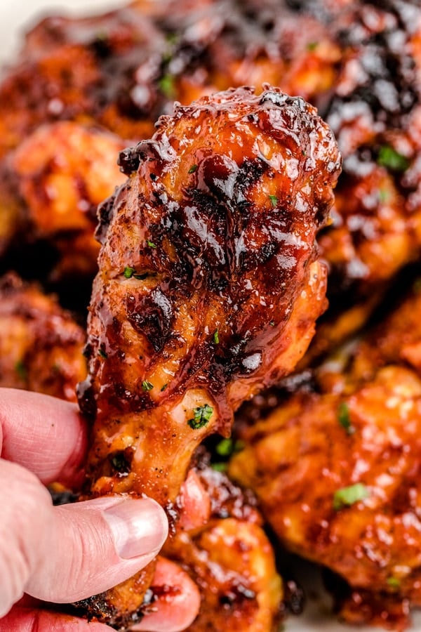 A close up picture of a piece of grilled BBQ chicken being held with a hand.