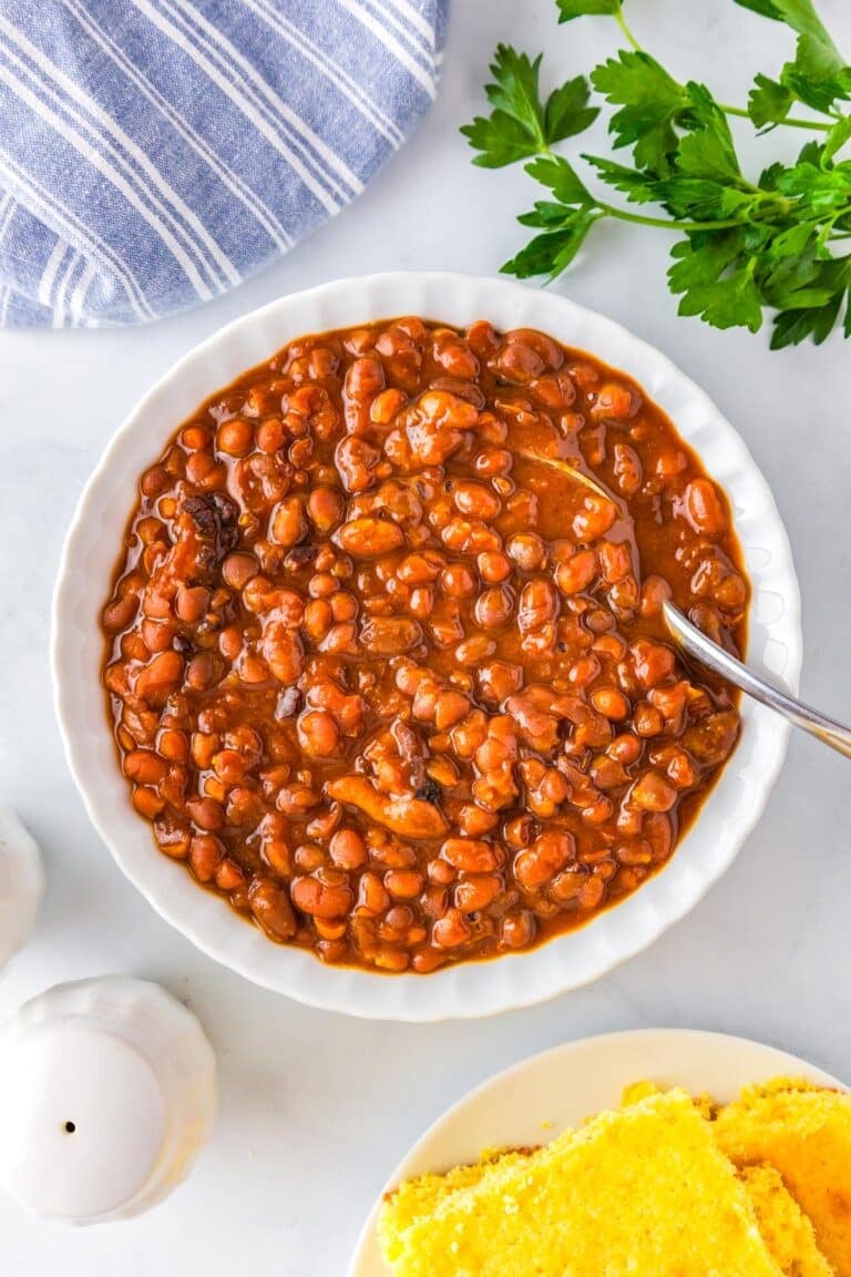 An overhead picture of a bowl of Boston baked beans with a serving spoon in them.