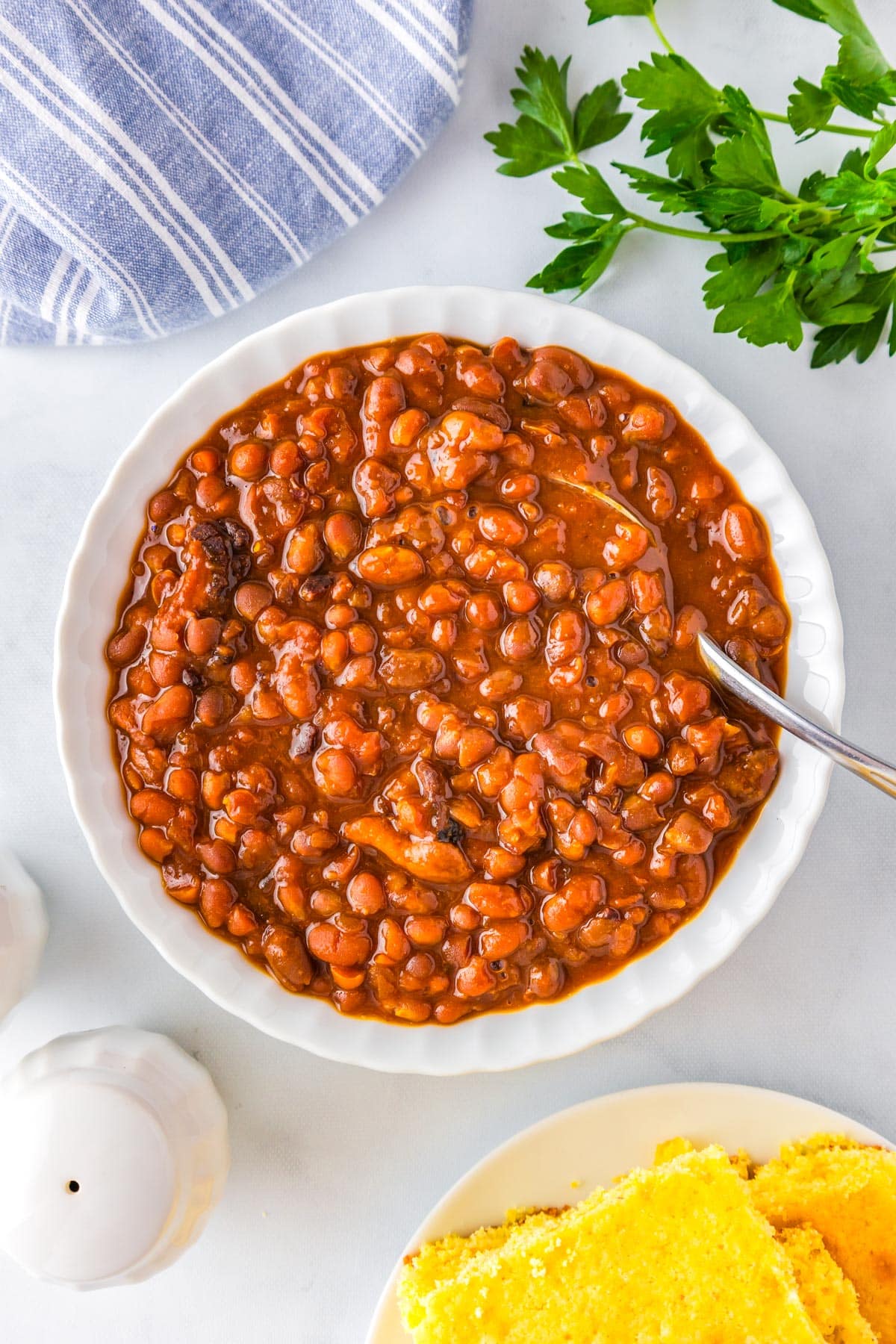 An overhead picture of a bowl of Boston baked beans with a serving spoon in them.