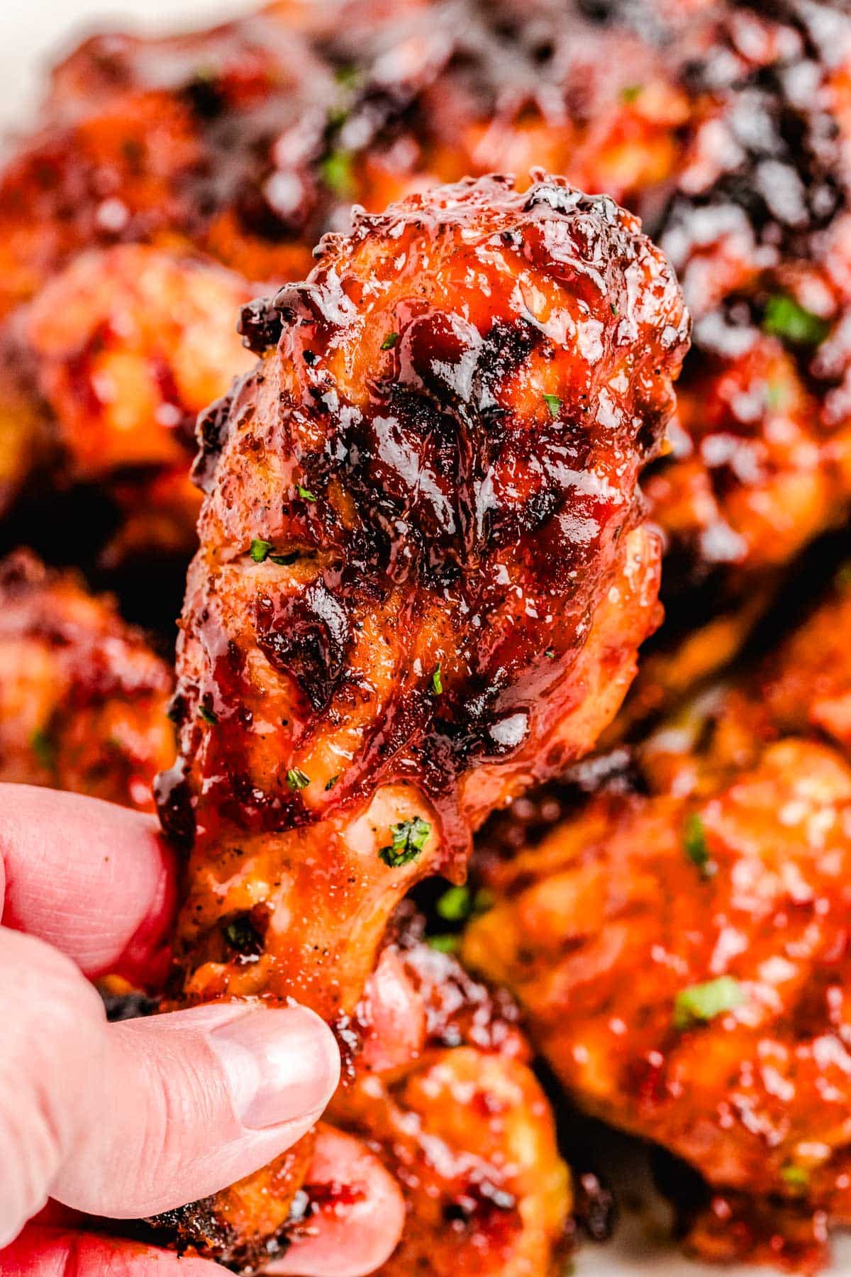 A hand picking up a piece of chicken grilled on a BBQ.