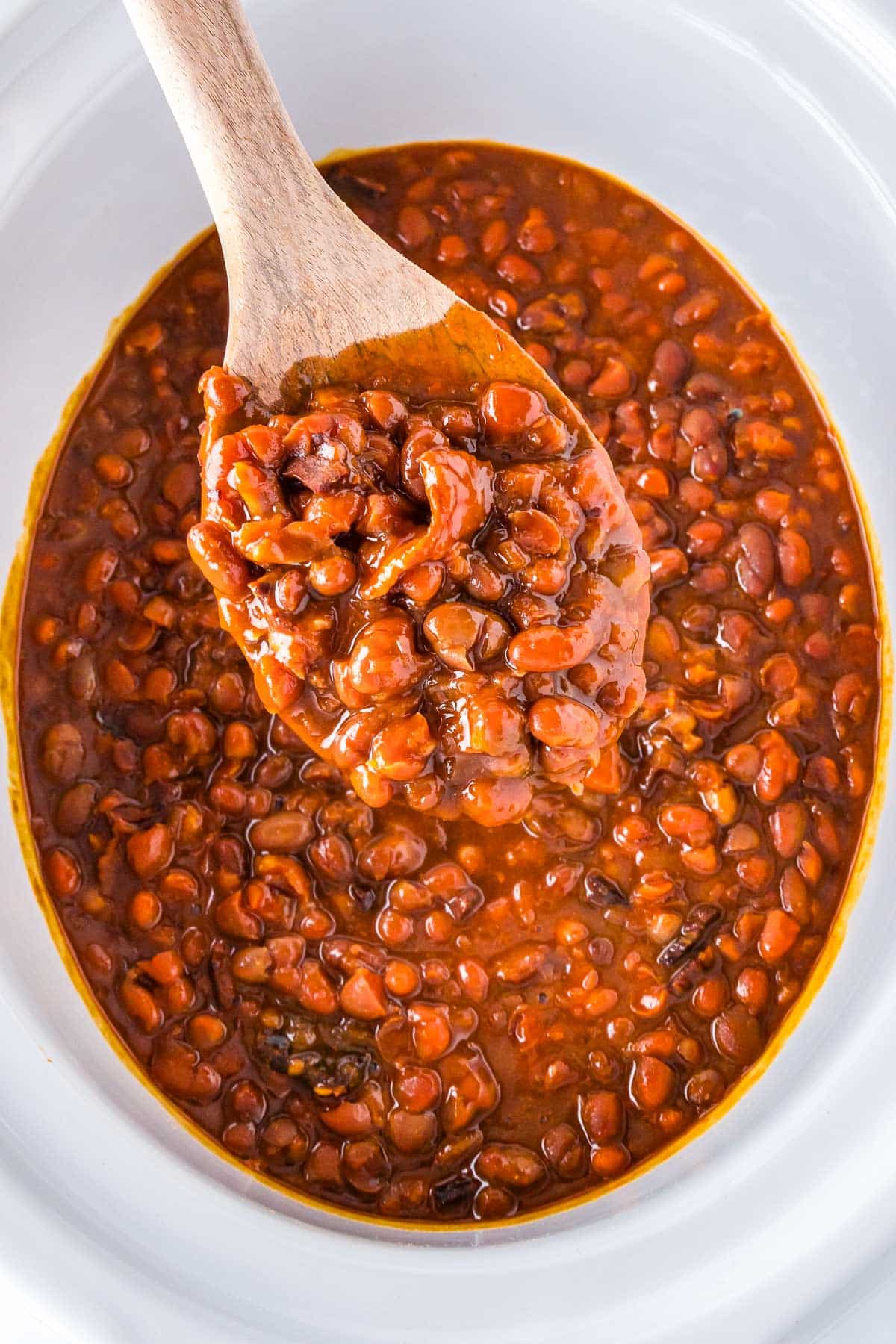 A wooken spoon picking up some of the finished crockpot baked beans.