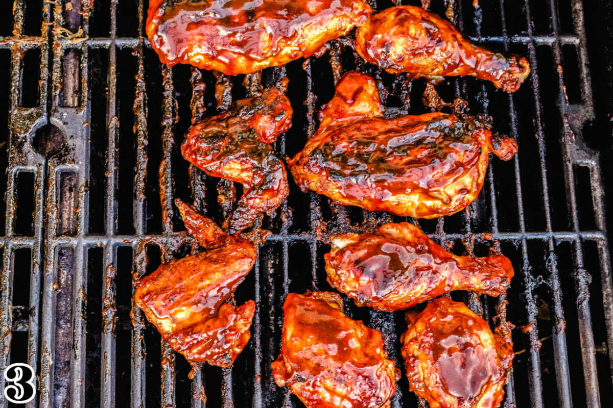 The chicken pieces cooking on the grill with BBQ sauce on them.