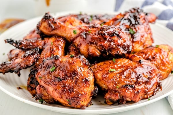 Close up picture of grilled pieces of BBQ chicken stacked on a white plate.