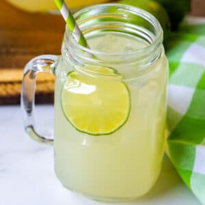 The finished limeade recipe in a clear glass mug with a paper straw.