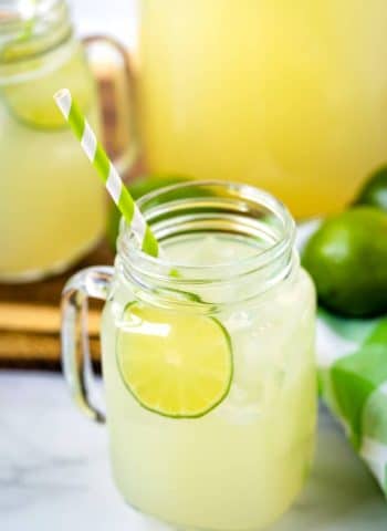 Limemade in a glass jar with a lime and paper straw.